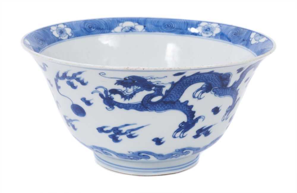 Lot 129 - Fine Chinese blue and white bowl, Kangxi period, of round form with straight foot and flared rim, decorated with dragons chasing flaming pearls, amongst stylised clouds and waves, prunus flowers on...