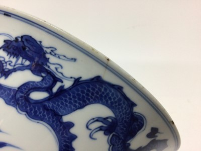 Lot 129 - Fine Chinese blue and white bowl, Kangxi period, of round form with straight foot and flared rim, decorated with dragons chasing flaming pearls, amongst stylised clouds and waves, prunus flowers on...