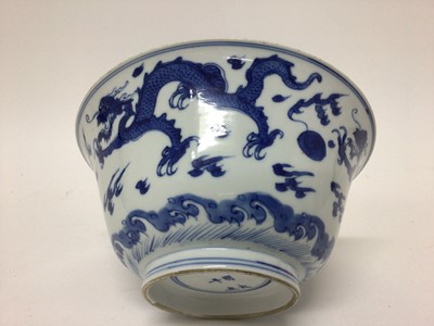 Lot 129 - Fine Chinese blue and white bowl, Kangxi period, of round form with straight foot and flared rim, decorated with dragons chasing flaming pearls, amongst stylised clouds and waves, prunus flowers on...