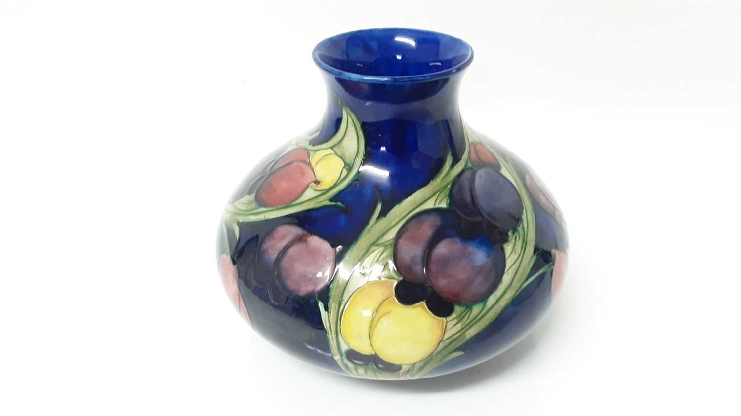 Lot 1201 - Moorcroft pottery vase with fruit decoration on blue ground, impressed marks to base with blue painted signature and original paper label - Potter To H.M The Queen, 17cm high