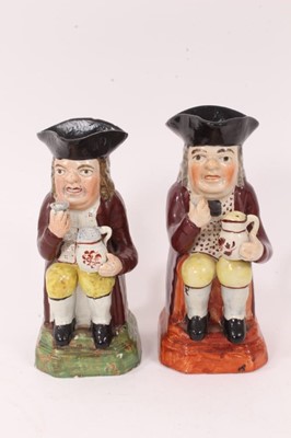 Lot 9 - Two Pearlware Toby jugs, early 19th century, both shown seated, each holding glass of beer in one hand and frothing jug of beer in the other, with red jackets, patterned shirts and yellow breeches,...