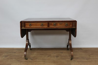 Lot 1457 - Good Regency rosewood and brass mounted sofa table, with rounded rectangular drop leaf top and two frieze drawers, each with lion mask handles  raised on standard ends and splayed legs terminating...