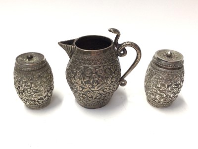 Lot 132 - Eastern white metal cream jug with floral scroll and bird decoration, together with similar pair of pepperettes