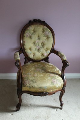 Lot 1219 - Victorian carved rosewood framed open arm chair with carved floral cresting upholstered in buttoned floral silk material, padded open arms on cabriole legs terminating on casters
