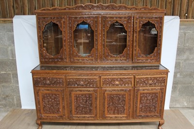 Lot 1411 - Highly ornate Anglo-Indian carved hardwood suite of dining furniture, comprising rounded rectangular dining table on trestle base, 205 x 123cm, set of six high back chairs and sideboard with glazed...