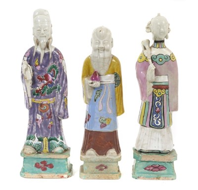 Lot 148 - Three Chinese porcelain figures of immortals, Qianlong period, each polychrome decorated and shown standing on square bases, the largest measuring 24cm high