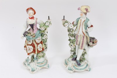 Lot 233 - A pair of Derby figural candlesticks, late 18th century, each standing next to floral encrusted tree trunks, on scrollwork bases, 26cm high
