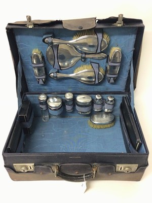 Lot 342 - Edwardian silver mounted cut glass travelling vanity set, comprising hand mirror, four brushes, seven silver topped bottles, another silver topped brush and other items, in a navy in leather case.