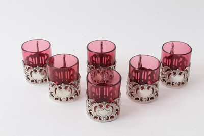 Lot 225 - Set six Edwardian silver mounted ruby glass beakers with rococo and cherub decoration, (Chester 1906), 6cm high