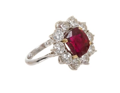 Lot 450 - Ruby and diamond cluster ring with an oval mixed cut ruby measuring approximately 9.1mm x 8.3mm x 6.1mm surrounded by a border of ten brilliant cut diamonds in claw setting on 18ct white gold shank...