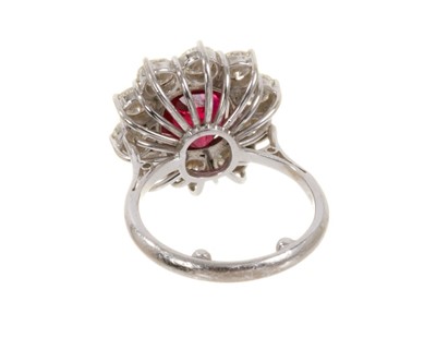 Lot 450 - Ruby and diamond cluster ring with an oval mixed cut ruby measuring approximately 9.1mm x 8.3mm x 6.1mm surrounded by a border of ten brilliant cut diamonds in claw setting on 18ct white gold shank...