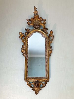 Lot 1062 - 18th century Venetian gilt wood pier mirror, with arched mirrored plate in C- scroll rococo frame with shell surmount, 80 x 33cm