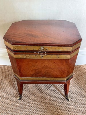Lot 1068 - George III mahogany and brass bound wine cooler, of canted rectangular outline with flanking lion mask handles and lead lined interior square tapered legs and castors, 52cm wide
