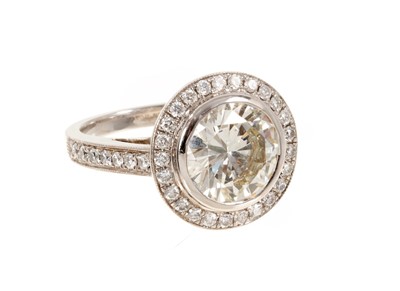Lot 692 - Fine diamond single stone ring, the round brilliant cut diamond weighing 3.38 carats, in a rub-over setting, surrounded by a border of twenty-five brilliant cut diamonds with fourteen diamonds to t...