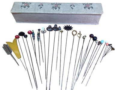 Lot 129 - Three Charles Horner hat pins- two with silver Welsh hat finials and one with a synthetic white stone, together with a collection of other vintage hat pins within a fabric embroidered fan box