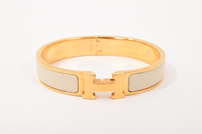 Lot 570 - Hermès bangle, the gilt bangle with signature logo 'H' clasp and cream enamel band, signed. In original Hermès pouch and box.