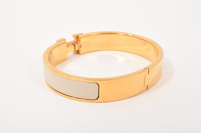 Lot 570 - Hermès bangle, the gilt bangle with signature logo 'H' clasp and cream enamel band, signed. In original Hermès pouch and box.