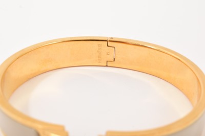 Lot 570 - Hermès bangle, the gilt bangle with signature logo 'H' clasp and cream enamel band, signed. In original Hermès pouch and box.