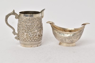 Lot 526 - Indian silver cream jug of barrel form, decorated in relief with animals under a foliate border, together with a similar ashtray, cream jug 8.4cm in overall height (2).