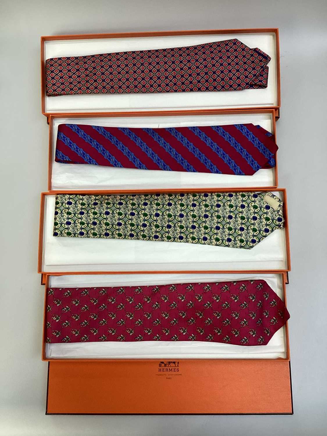 Lot 2084 - Four Hermès silk ties, Jockey riding ostrich 7987 EA, apples 7691 OA, linked horsebit 7248 MA and stylised tulip 7271 MA all in Hermes tie boxes with tissue paper.