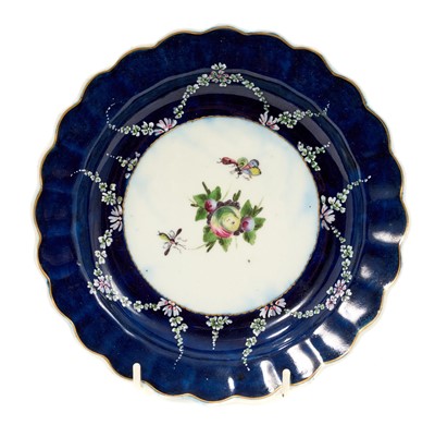 Lot 214 - An unusual Worcester scalloped plate, circa 1770, the centre enamelled with spotted fruit and two insects, with raised swag decoration outside, on wet blue ground, believed by John Sandon to hav...