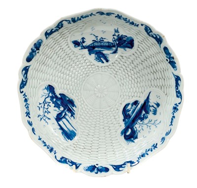 Lot 221 - A rare and early Worcester blue and white junket dish, circa 1758, painted with three landscape panels in the Neighbours pattern on a basket-weave moulded ground, the shaped rim with flowers and...