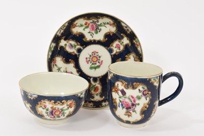 Lot 38 - A Worcester trio, circa 1760-70, comprising coffee cup, tea bowl and saucer, polychrome painted with floral sprays in gilt scrollwork panels, on a blue scale ground, square marks to bases