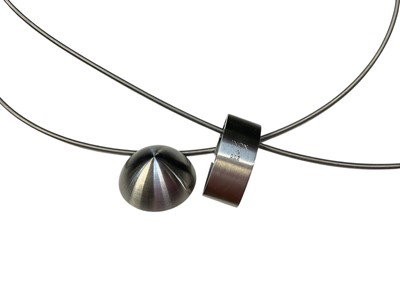 Lot 12 - Michael Birnie - contemporary diamond and stainless steel pendant on stainless steel wire cord necklace together with a similar Modernist gold and stainless steel pendant necklace (2)
