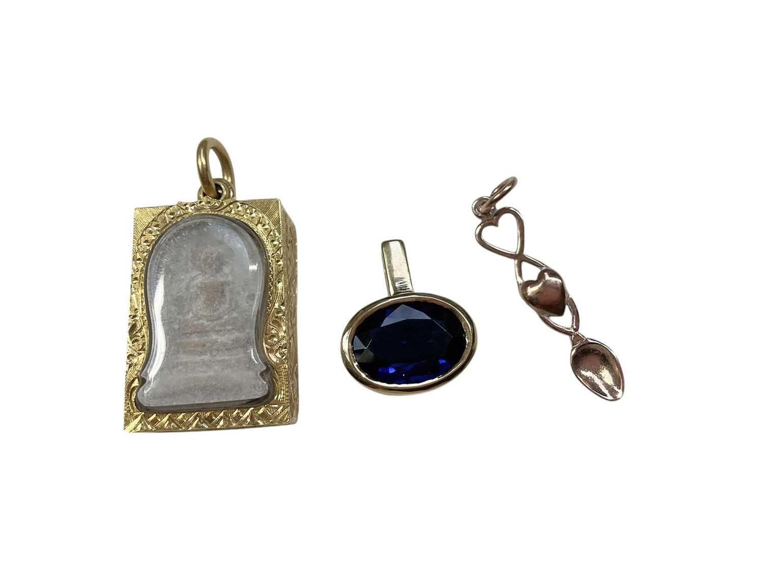 Lot 30 - Eastern religious tablet in yellow metal pendant setting, a blue stone pendant in 18ct gold setting and a 9ct rose gold Welsh love spoon pendant (3)