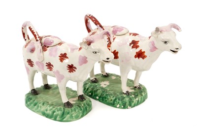 Lot 134 - A pair of early 19th century Swansea lustre cow creamers, painted with splashes of red and pink, on naturalistic green-painted bases, 18cm long