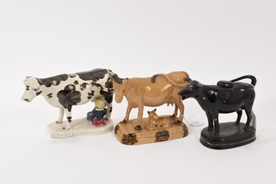 Lot 137 - A mid 19th century English pottery cow creamer with milkmaid, polychrome painted, together with a black-glazed creamer and a buff-glazed model of a cow and calf with brown splash decoration (3)