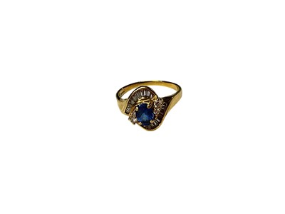 Lot 215 - Sapphire and diamond cluster ring with a oval mixed cut blue sapphire measuring approximately 7mm x 5mm flanked by four brilliant cut diamonds in a gold crossover setting with channel set baguet...