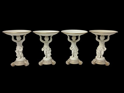 Lot 6 - Set of four 19th century white glazed tazzas, each in the form of a circular dish being held aloft by a putto, the bases decorated in gilt, 24.5cm high