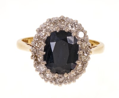 Lot 551 - Sapphire and diamond cluster ring with an oval mixed cut blue sapphire surrounded by a border of brilliant cut diamonds in claw setting on 18ct gold shank