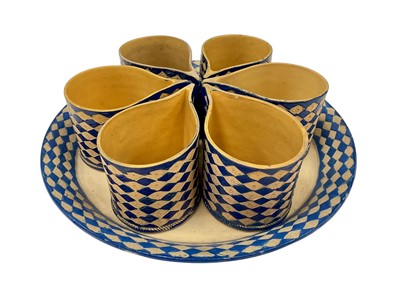 Lot 4 - Rare Staffordshire caneware custard set, circa 1800, comprising tray and six cups, with impressed lozenge pattern, painted in blue enamel, the tray 20cm diameter