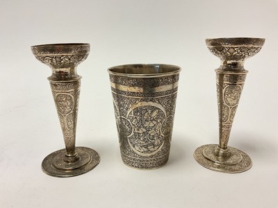 Lot 7 - Middle Eastern white metal trio, consisting of a pair of spill vases and a beaker, with engraved figural decoration on a foliate patterned ground, each piece marked to base, the vases 14.5cm hig...