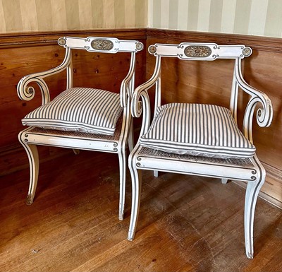 Lot 1574 - Pair of Regency-style white painted and parcel gilt open elbow chairs with cane seats on sabre legs, with striped fabric cushions