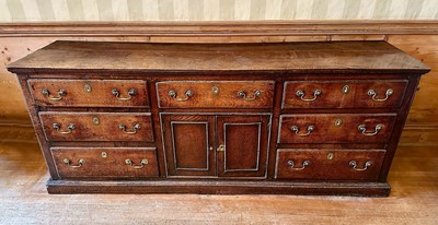 Lot 1575 - George III oak dresser base with an arrangement of seven drawers around central twin cupboards, with brass swan neck handles, on plinth base, 196cm wide x 52cm deep x 76cm high