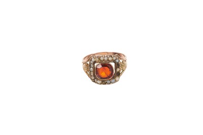 Lot 653 - George III garnet and seed pearl ring with a cushion cut garnet surrounded by a border of seed pearls on gold acanthus leaf shoulders to a reeded and tapered gold shank, ring size J½.