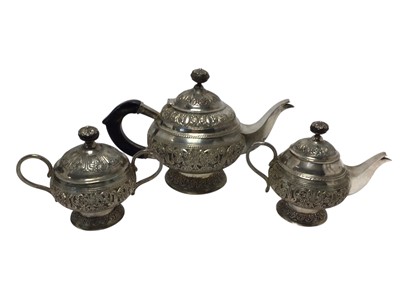 Lot 497 - Early 20th century Anglo Indian white metal three piece teaset comprising teapot of cauldron form with embossed decoration, domed hinged cover with horn finial and horn handle, raised on a circu...