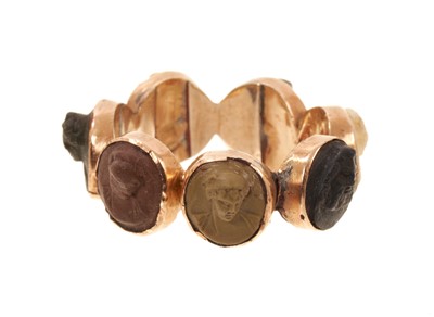 Lot 409 - Early 19th century carved lava cameo ring with a band of seven lava cameos carved in high relief depicting classical busts, in gold setting