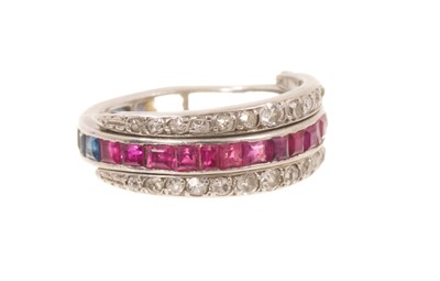 Lot 414 - Art Deco diamond, ruby and sapphire eternity ring with a central band of calibre cut rubies to one half and sapphires to the other, flanked by two hinged bands of graduated old cut and single cu...