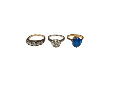 Lot 69 - 18ct gold five synthetic white stone ring in carved scroll setting, size M½, synthetic white single stone ring in platinum setting, size M and a yellow metal single blue stone ring, size K½ (3)