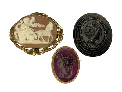 Lot 84 - Three Victorian cameo brooches to include a carved shell cameo depicting a boy on a goat pulled chariot in a gilt metal mount, amethyst glass cameo depicting a classical female bust and one othe...