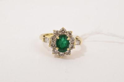 Lot 280 - Emerald and diamond cluster ring with a central oval mixed cut emerald surrounded by a border of brilliant cut diamonds and two further baguette cut diamonds to the shoulders, in a yellow gold s...