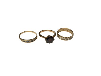 Lot 258 - 9ct gold garnet single stone ring, 9ct gold synthetic white stone eternity ring and a yellow metal gem set ring (3)