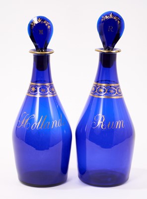 Lot 318 - Pair of Georgian Bristol blue glass spirit decanters, each with gilt decoration and naming 'Rum' and 'Hollands', together with matching target stoppers with similar decoration, each 25cm in heig...