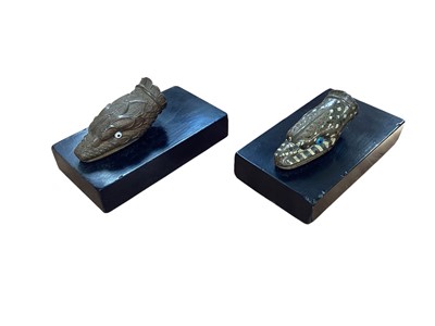 Lot 5009 - Unusual near pair of cast metal heads of serpents/beasts, one with scales, the other with foliate and enamelled decoration, each with glass eyes, on black plinth bases, the heads 7.75cm long