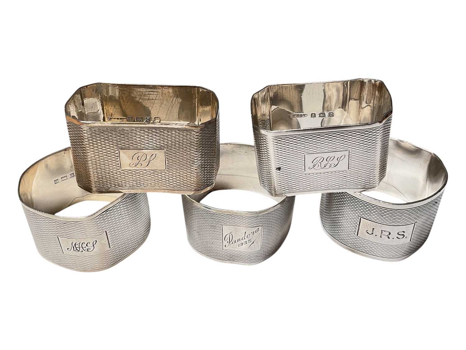 Lot 129 - Five various silver napkins rings with engine turned decoration and engraved initials/names