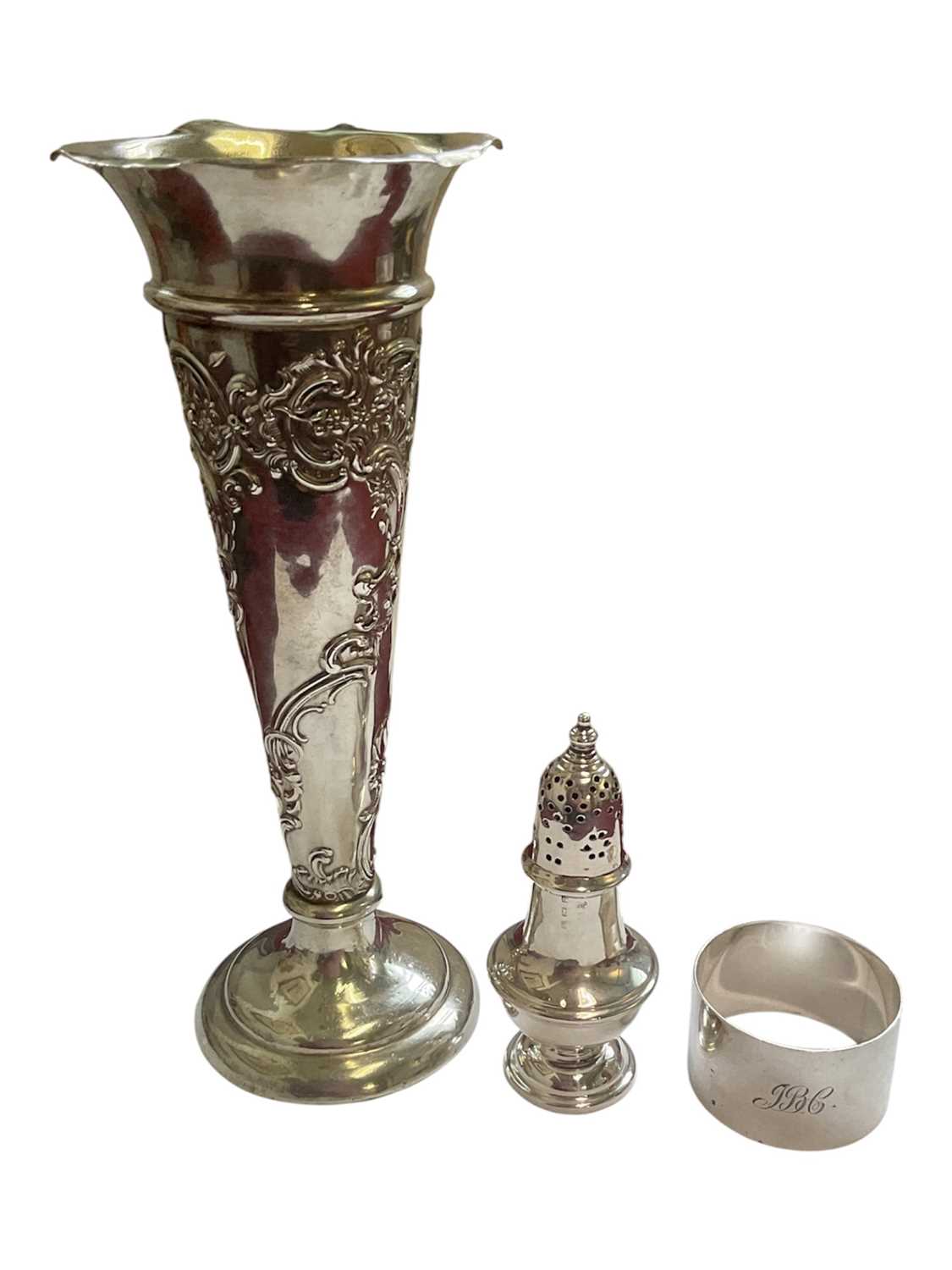 Lot 86 - Edwardian silver spill vase with embossed floral scroll decoration, silver napkin ring and a silver pepperette with weighted base (3)